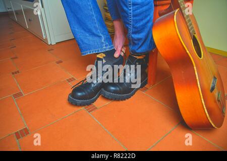 Rock und Roll Konzept. Schwarze Stiefel und akustischer Gitarre. Das Setzen auf Rock und Roll Stiefel Stockfoto