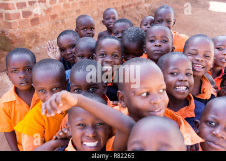 Eine Gruppe von Happy Grundschulkinder lächeln, lachen und winken. Sie sind in der Schule Uniformen gekleidet. Stockfoto
