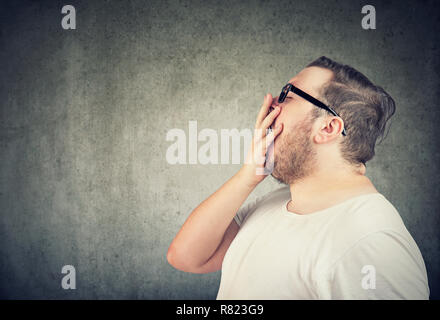 Seitenansicht des mollig Mann im weißen T-Shirt und Brillen, Mund, während das Gähnen auf grauem Hintergrund Stockfoto