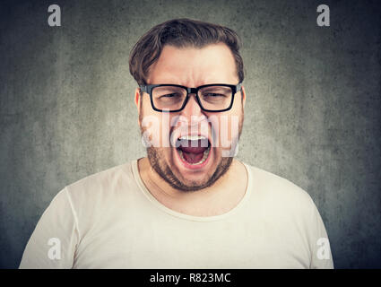 Junge casual mollig Mann in Gläsern an Kamera kreischen im Zorn auf grauem Hintergrund Stockfoto