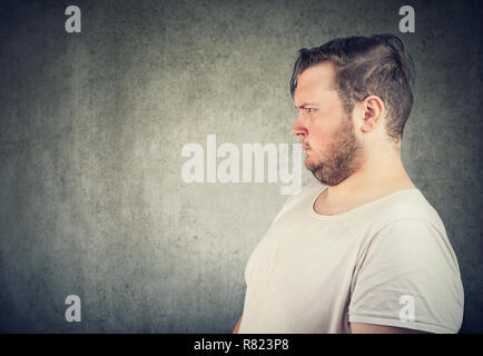 Seitenansicht von Übergewicht legerer Mann in Ärger und Ekel auf grauem Hintergrund Stockfoto