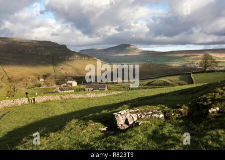 Spaziergänger durchqueren ein Stil an wharfe Holz, in der Nähe von Feizor, mit Pen-y-Ghent peak in Ribblesdale am Horizont. Yorkshire Dales National Park. Stockfoto