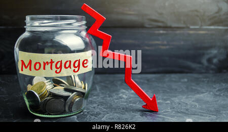 Glas Glas mit Münzen und die Inschrift 'Durch Hypotheken' und dem Pfeil nach unten. Weniger Interesse an der Hypothek. Niedrige Zinsen. Fallende Immobilienpreise. Stockfoto