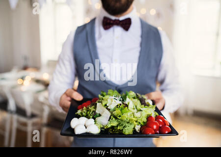 Mittelteil der Mann stand im Innenraum in einem Zimmer für eine Partei, die ein Tablett mit Gemüse. Stockfoto