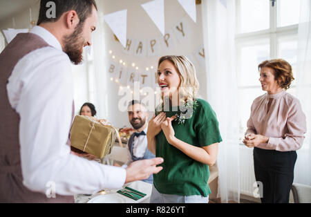 Ein Mann, der ein Geschenk überrascht junge Frau auf einer Geburtstagsfeier in der Familie. Stockfoto