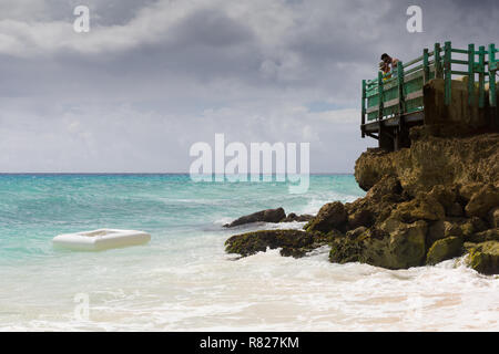 Eine weggeworfene Kunststoff Rettungsinsel wäscht bis auf den Felsen auf der karibischen Insel Barbados während Urlauber bei einem Resort Hotel Blick auf. Stockfoto