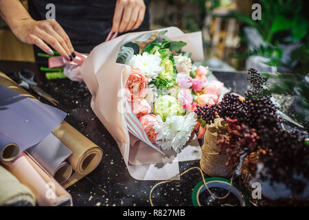 In der Nähe von wunderschönen bouqette von Blumen liegen auf dem Tisch. Es gibt Rollen Papier und Blumen. Frau touch Blumenstrauß mit Händen. Stockfoto