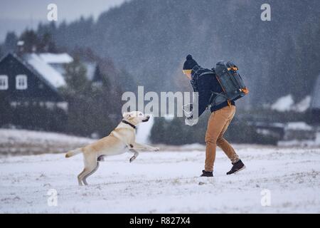 Freundschaft zwischen Tierhalter und seinem Hund. Junge Mann spielt mit Labrador Retriever im Winter Landschaft. Isergebirge, Tschechien