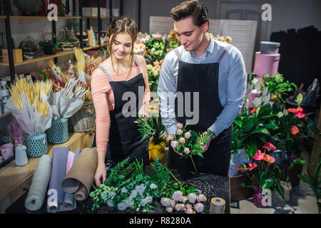 Attraktive junge weibliche und männliche Blumenhändlern Blumensträuße erstellen und an einander. Sie lächeln. Kerl halten boueut in Händen. Stockfoto