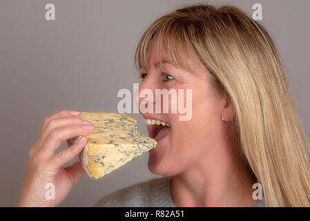 Blonde Frau essen und genießen Sie ein Keil der blauen Käse Stockfoto