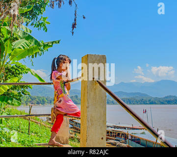 Ein kleines Mädchen lehnte sich auf dem Geländer durch ein Dorf am Mekong River sieht und denkt, 'Eines Tages mein Schiff wird kommen' Stockfoto