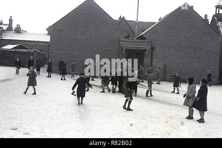 1950, historische, Winter und Schulkinder in den Mänteln Spaß spielen draußen im Schnee Schule Spielplatz, England, UK. Stockfoto