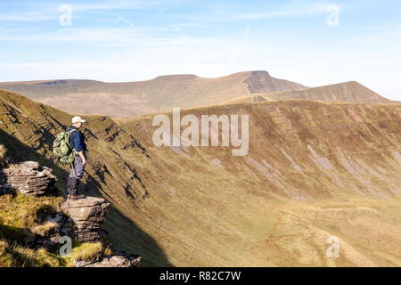 Ein Wanderer auf einem Felsvorsprung aus Rock, nimmt im Hinblick auf die höchsten Gipfel in den Brecon Beacons National Park, Pen Y Fan und Mais Du Stockfoto