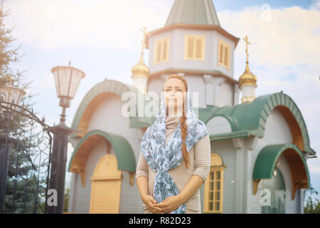 Russisch-orthodoxe Frau mittleren Alters in einem Schal steht auf dem Hintergrund der Orthodoxen Kirche aus Holz. Stockfoto