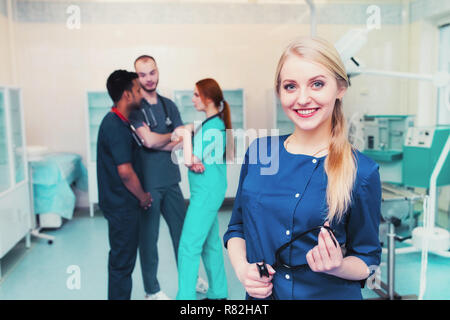 Blonde junge Chirurgen in die Kamera lächelnd mit einem Team von gemischten Rennen Medizinstudenten an der Universität. Stockfoto