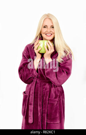 Attraktive Frau in Lila flauschigen Morgenmantel Hände halten um eine Tasse Tee, gegen weiße Hintergrund Stockfoto