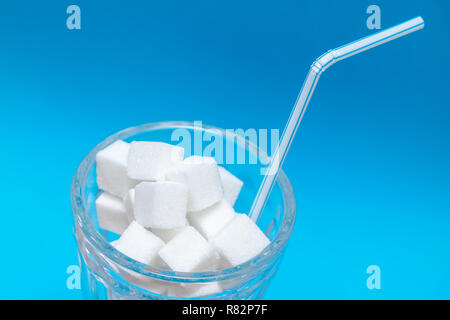 Glas voll Würfelzucker mit Getränk Stroh auf blauem Hintergrund - ungesunde Ernährung Konzept. Stockfoto
