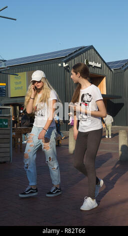 Junge Mädchen oder Teenager zusammen gehen, während ein Gespräch über Ihr Mobiltelefon ist, stilvolle Street Fashion bei V&A Waterfront in Kapstadt Stockfoto