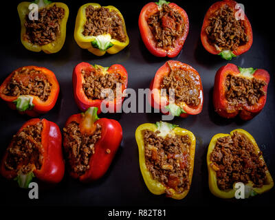 Rote und gelbe Paprika halbieren, mit Hackfleisch, Fleisch und gebacken, auf schwarzem Hintergrund Stockfoto