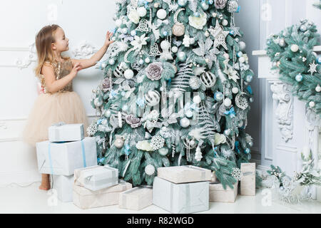 Kleines Mädchen in einem schönen Kleid hängt, Dekorationen auf den Weihnachtsbaum. Stockfoto