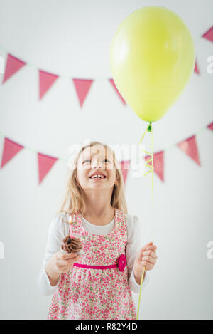 Schöne glückliche kleine Mädchen mit Ballon und kleinen Geburtstagskuchen mit Kerze. Stockfoto