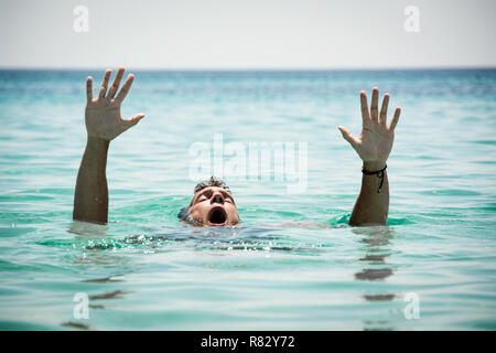 Ertrinkenden im Meer um Hilfe zu bitten, mit erhobenen Armen. Stockfoto