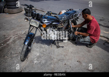 Caracas, Venezuela. 11 Dez, 2018. Eine venezuelanische Reparaturen der Reifen eines Motorrades. Angesichts der Wirtschaftskrise, alles, was in Venezuela wird repariert, bis es vollkommen nutzlos ist. Die venezolanische Inland leidet unter der Wirtschaftskrise. Nach Angaben des Internationalen Währungsfonds (IWF), der Südamerikanischen Land ist die Überschrift für die Inflationsrate von 1,37 Millionen Prozent im Jahr 2018. Credit: Rayner Pena/dpa/Alamy leben Nachrichten Stockfoto