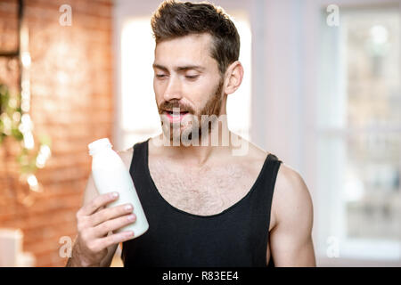 Schöner sport Mann in Schwarz t-shirt mit Milch Flasche zu Hause Stockfoto