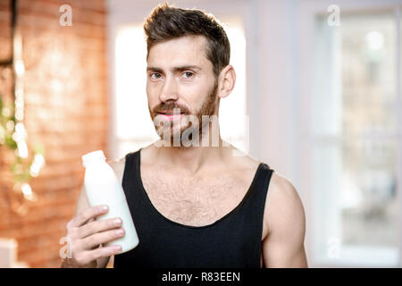 Schöner sport Mann in Schwarz t-shirt mit Milch Flasche zu Hause Stockfoto