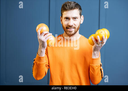 Bunte Porträt einer kaukasischen bärtigen Mann in Orange Pullover holding Früchte auf dem blauen Hintergrund Stockfoto