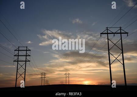 Silhouette des Stromnetzverteilernetzes, Strommasten und Hochspannungsleitungen, die bei Sonnenuntergang in den fernen Horizont übergehen Stockfoto