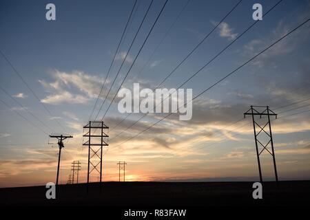 Silhouette des Stromnetzes, elektrischer Übertragungsmast und Hochspannungsleitungen, die bei Sonnenuntergang in den fernen Horizont übergehen Stockfoto