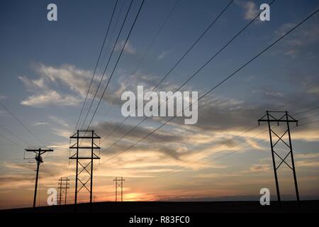 Silhouette des Stromnetzverteilernetzes, Strommasten und Hochspannungsleitungen, die bei Sonnenuntergang in den fernen Horizont übergehen Stockfoto