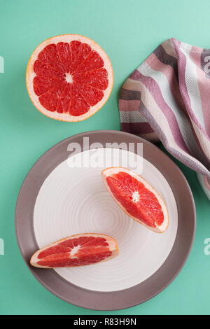 Zwei pampelmusen Scheiben auf einen Teller, gestreifte Serviette gegen türkis Tabelle. Minimal Style trendigen Pastellfarben. Gesunde Lebensweise. Stockfoto