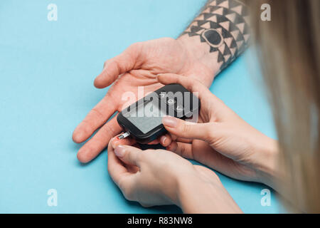 Nahaufnahme Blick auf Frau testen Mann Blutzuckerspiegel mit glucometer auf blauem Hintergrund Stockfoto