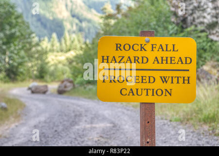 Dieses Schild in Mt. Rainier National Park warnt Wanderer, dass Sie sich in einem explosionsgefährdeten Bereich. Riesige, gefallene Felsbrocken Wurf die Straße im Hintergrund. Stockfoto