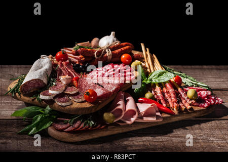 Schneidbretter mit leckeren Salami, geräucherte Würste, Schinken, Gemüse und Kräutern auf Holz- rustikalen Tisch Stockfoto