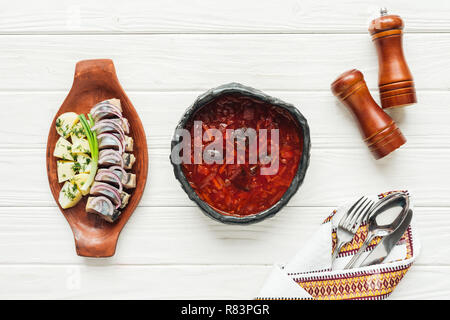 Blick von oben auf die traditionellen Rote-Bete-Suppe mit Hering und Besteck auf weißem Holz- Hintergrund Stockfoto