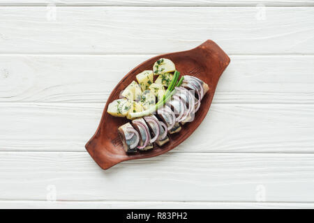 Blick von oben auf die marinierten Hering mit Kartoffeln und Zwiebeln aus Steingut Teller auf weißem Holz- Hintergrund Stockfoto