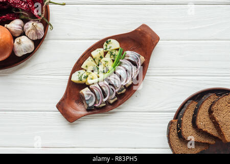 Blick von oben auf die marinierten Hering mit Kartoffeln und Zwiebeln aus Steingut Teller mit Roggenbrot auf weißem Holz- Hintergrund Stockfoto