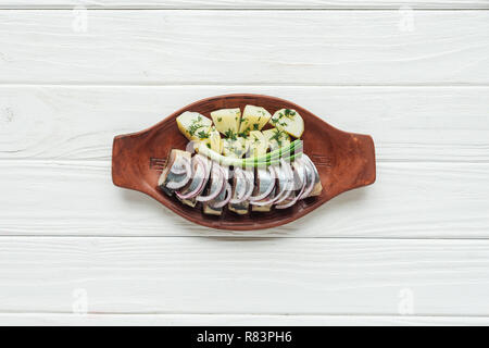 Blick von oben auf die marinierten Hering mit Kartoffeln und Zwiebeln aus Steingut Teller auf weißem Holz- Hintergrund Stockfoto