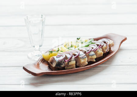 Marinierter Hering, Kartoffeln und Zwiebeln aus Steingut Teller mit Glas Wodka auf weißem Holz- Hintergrund Stockfoto