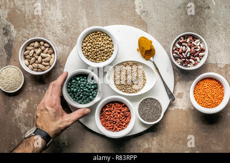 7/8-Ansicht von Mann mit Spirulina mit Superfoods und Leguminosen auf strukturierte rustikalen Hintergrund Stockfoto