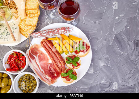 Italienische Antipasti Wein Snacks. Antipasti, Salami, Käse, Trauben, Oliven, Gurken, Schinken mit Melone, Brushettas auf grunge grauen Hintergrund. Es Stockfoto