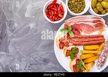 Italienische Antipasti Wein Snacks. Antipasti, Salami, Käse, Trauben, Oliven, Gurken, Schinken mit Melone, Brushettas auf grunge grauen Hintergrund. Es Stockfoto