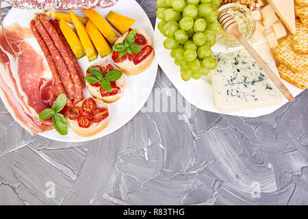 Italienische Antipasti Wein Snacks. Antipasti, Salami, Käse, Trauben, Oliven, Gurken, Schinken, Melone, Brushettas auf grunge grauen Hintergrund. Italienisch Stockfoto