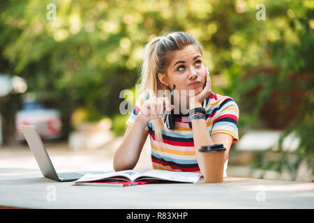 Bild eines Denkens nachdenkliche junge süße Mädchen student sitzt im Park mit Laptop Computer schreiben. Stockfoto