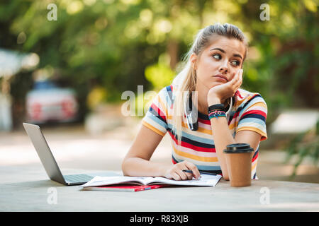 Bild von einem müden jungen Mädchen Schüler sitzt im Park mit Laptop Computer schreiben. Stockfoto