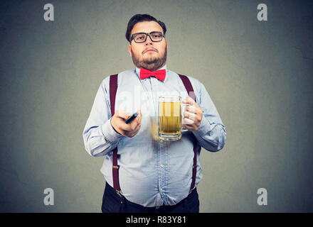 Nach faul beleibten Mann in formalen Outfit holding Krug Bier und Fernsehen auf grauem Hintergrund Stockfoto