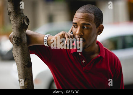 Mitte der erwachsene Mann stand neben einem Baum an einem Handy. Stockfoto